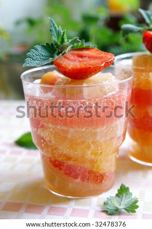 A glass of cooling citrus (lemon, orange, grapefruit) drink decorated with fresh strawberry and mint leaves, green blur background, closeup
