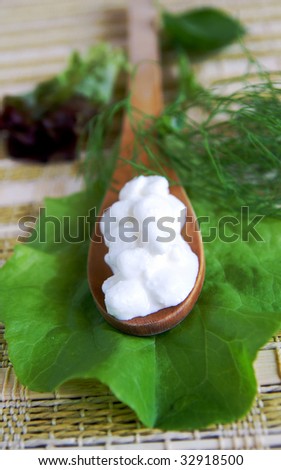 A wooden spoon with fresh cottage cheese on a green lettuce leaf, arranged with dill, basil and lettuce leaves, closeup, blur background, vertical