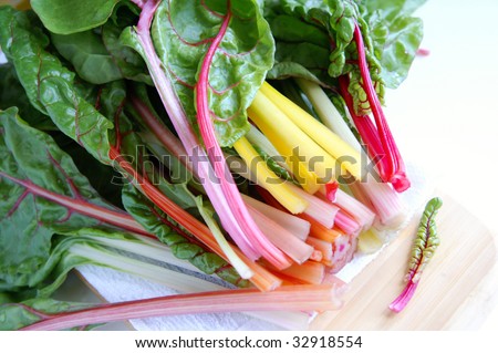 A bunch of fresh new chard crops of different colors on a white napkin and wooden kitchen board, white background, shallow depth