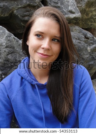 Beautiful young brown haired blue eyed woman poses in blue hoody sweatshirt in front of rock wall