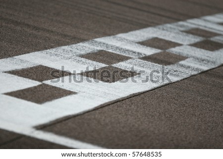 The painted start/finish line across the track at the Rockingham motor speedway in Northamptonshire, UK. Black tire marks are streaked across the track. Shallow focus is on the near part of the line.