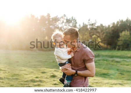 Happy family walking outdoor. Father holds child on hands and plays with him. They are happy together
