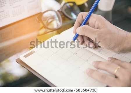 Close up of hands woman,she is writing something on calendar.On the desk have glasses calendar and notebook.