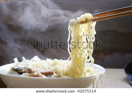 Chopsticks picking up rice noodles from a steaming hot bowl.