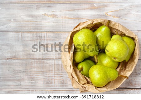 background with green pears in a paper bag on a white wooden background, top view.