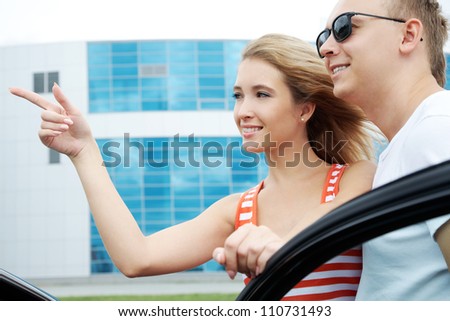 Attractive woman showing something to man and putting her hand on the door of car