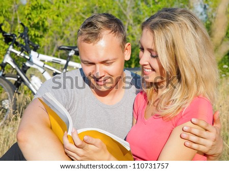 Handsome man embracing her girlfriend and reading together book outdoor