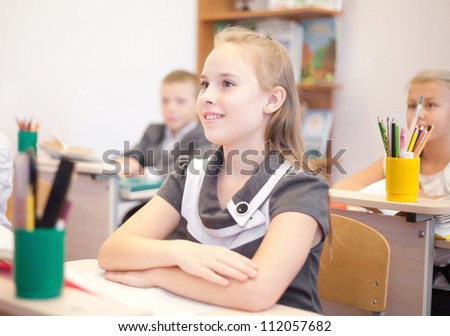 Children sitting at the table and looking at the teacher with focus on girl
