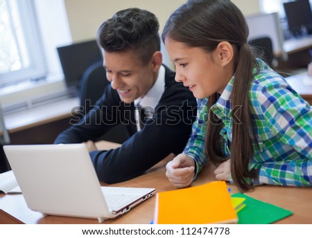 Young students chatting  and typing at laptop in the classroom