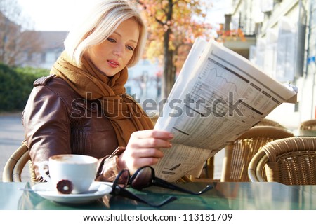 Attractive young business woman reading a newspaper at outdoor cafe