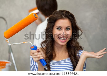 Pretty happy woman looking at camera while her husband painting wall