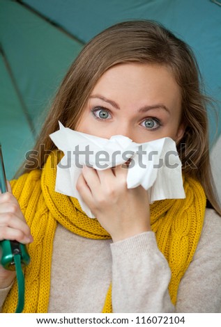 Sick woman holding umbrella and blowing her nose