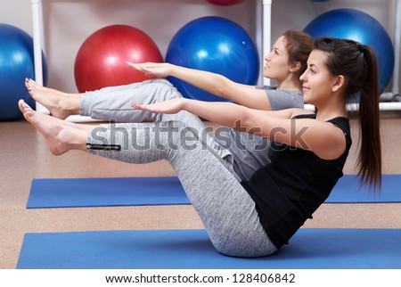 Two young women doing  exercise  on mates in gym