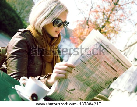 Smiling woman reading newspaper in the outdoor cafe