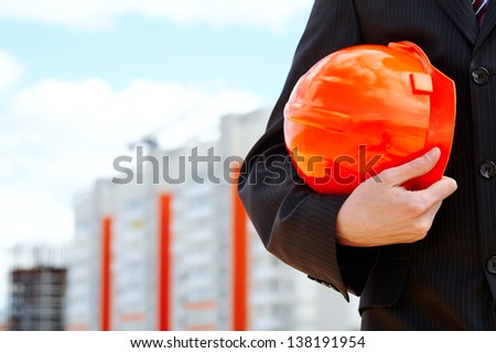 Close-up of businessman holding orange helmet over building construction