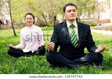 Businesspeople sitting on grass and doing yoga near building office