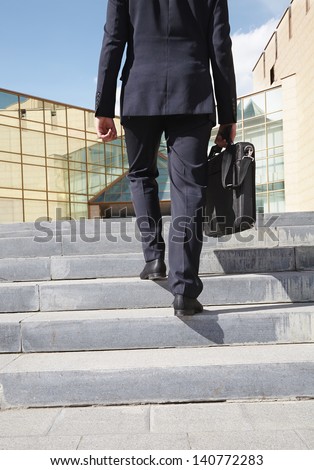 Close-up of confident businessman with briefcase walking upstairs