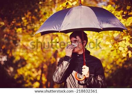 Sick man holding umbrella  and  blowing nose at autumn day