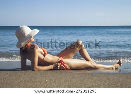 Fit woman in bikini and hat relaxing on seashore
