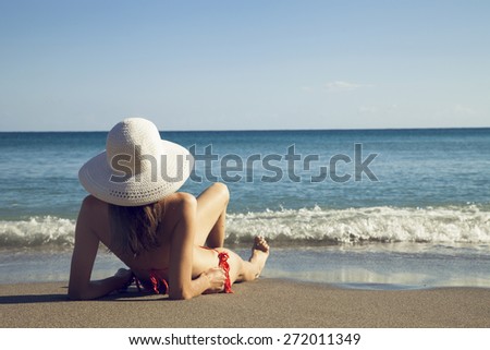 Fit woman in bikini and hat relaxing on seashore