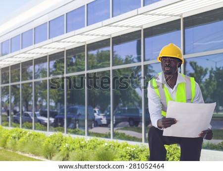 Serious worker architect in hardhat holding design project near modern building