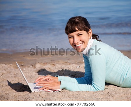 Happy young woman working on laptop at the sea beach