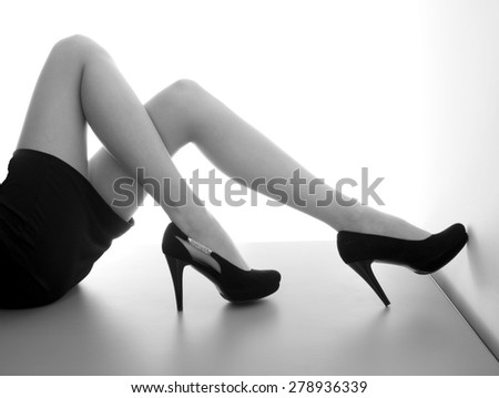 Female legs in high heels on a white background, table with reflections, black and white