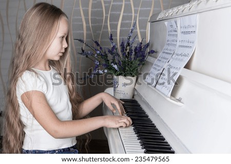 Portrait of little girl in white dress playing piano. Concept of music study and arts