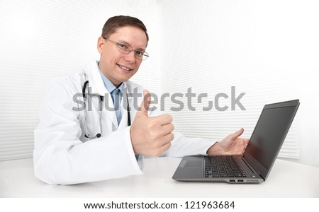 Doctor with laptop sitting in doctor\'s office and showing his thumb up