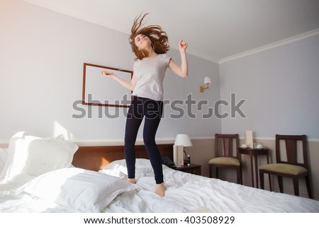 Carefree girl jumps on the bed while listening pop music