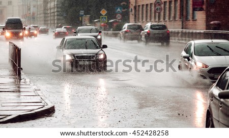 Fast speed. Moving car sprays puddle when heavy rain drops on concrete. Wide screen