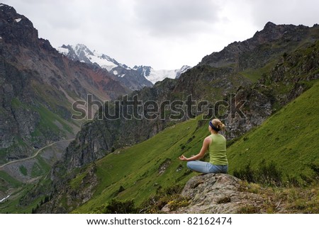 The young girl makes meditation in beautiful mountain gorge. Snow tops are in the distance visible