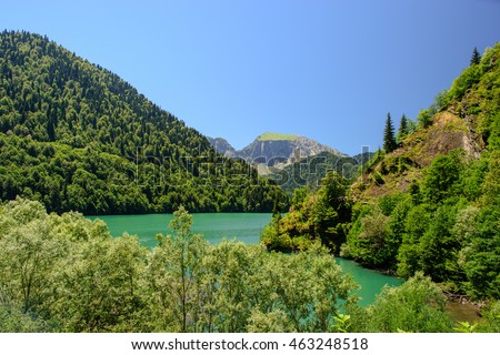 Amazing nature landscape view of lake with incredible color of water surrounded by peaks of mountain forest and blue sky as a background. Natural scenery of high ground and green trees growing on it.