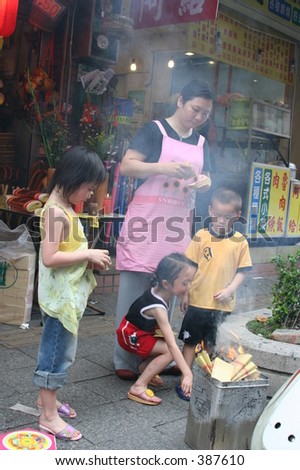 mother and children burning paper money on the sidewalk at the occasion of celebrating the birthday of a deity in Danshui, Taiwan