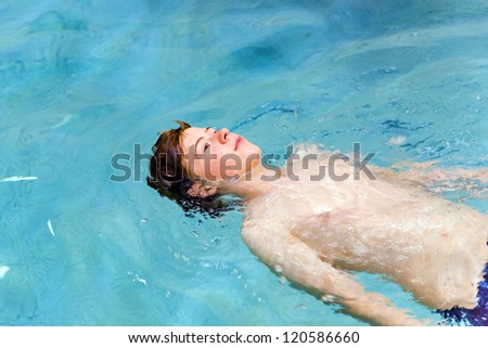 boy with red hair enyoing swimming in an indoor pool and lying on the back