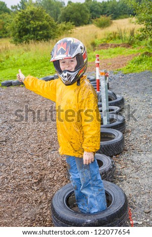 happy boy with helmet at the kart trail in rain with dirty face and clothing