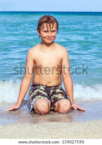 boy sits at the beach and plays with his hands in the water