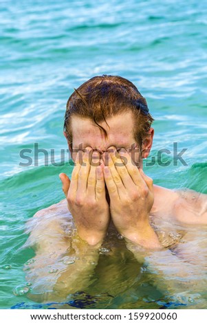teenage boy cleans eyes of saltwater in the ocean
