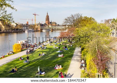 FRANKFURT, GERMANY - MARCH 29: people enjoy the first warm spring day on March 29, 2014 in Frankfurt, Germany. They relax at river Main with view to Skyline of Frankfurt.
