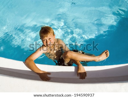 happy cute boy in swimming pool laughes and poses
