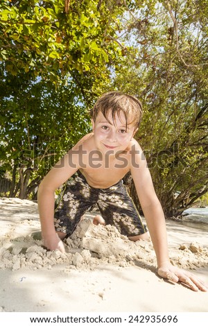 happy young boy is digging in the sand of the beach and constructing sand buildings
