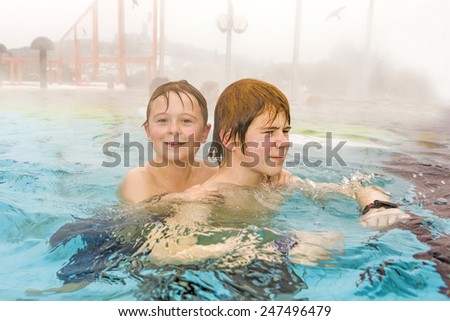 brothers are swimming in the outside area of a thermic pool in Wintertime in warm water, it is foggy