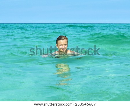handsome teen has fun swimming in the ocean under blue sky