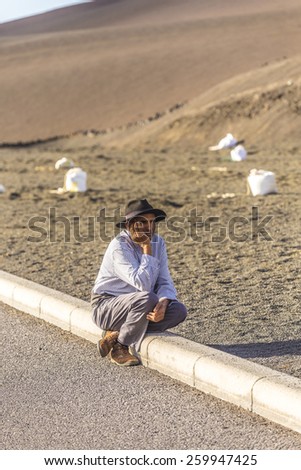 YAIZA, SPAIN - NOV 15, 2014: local camel riding man sits down and waits for tourists in Yaiza, Spain. Camel riding in Timanfaya national park is a must for tourists in Lanzarote.