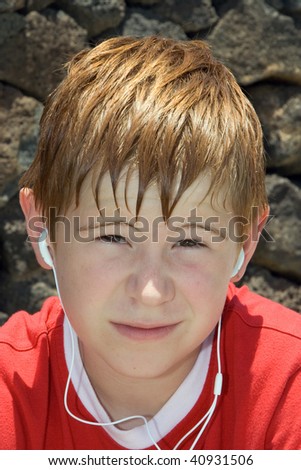 boy, child with red hair is listening the music from the earphones and is looking annoyed