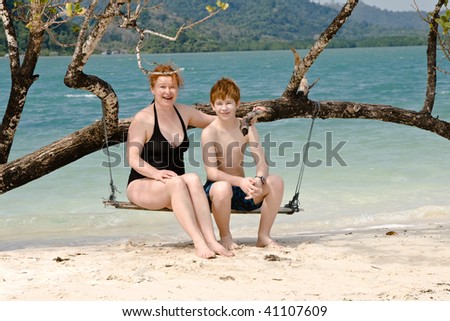 mother and son sitting on a beautiful swing, relaxing on a idyllic beach like paradise