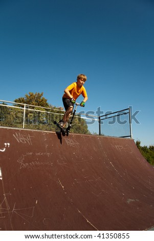 child, boy is jumping with a scooter over a quarter pipe in the skate parc and enjoying it