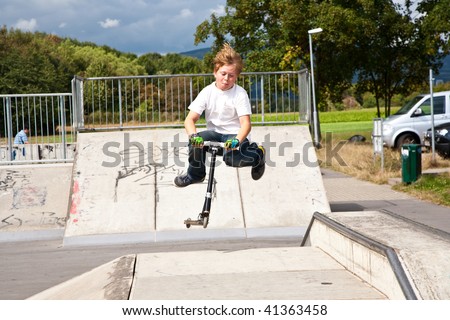 child, boy is jumping with a scooter over a fun box in the skate parc and enjoying it