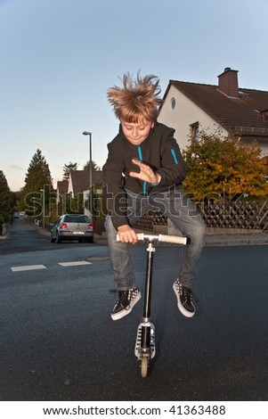child, boy is doing tricks, jumping with a scooter on the street and having fun and enjoying it