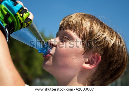 boy is sweating and thirsty from doing sports and drinks mineral water out of a bottle